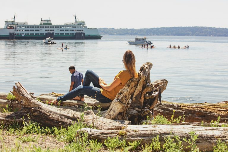 woman sitting near a lake watching a boat